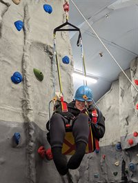 Young person climbing a climbing wall wearing a harness and hardhat
