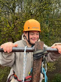 Young person climbing a climbing frame wearing a harness and hardhat