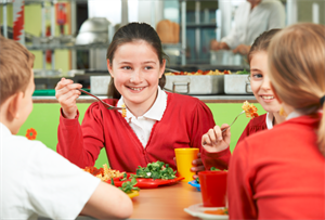 Young people wearing school uniform eating lunch around a table